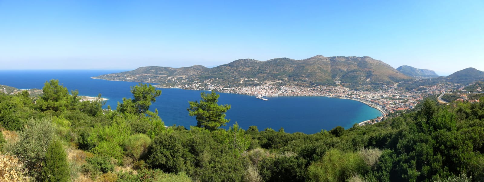 Ampia vista su una baia di Samos con pendii boscosi ed edifici lungo la costa