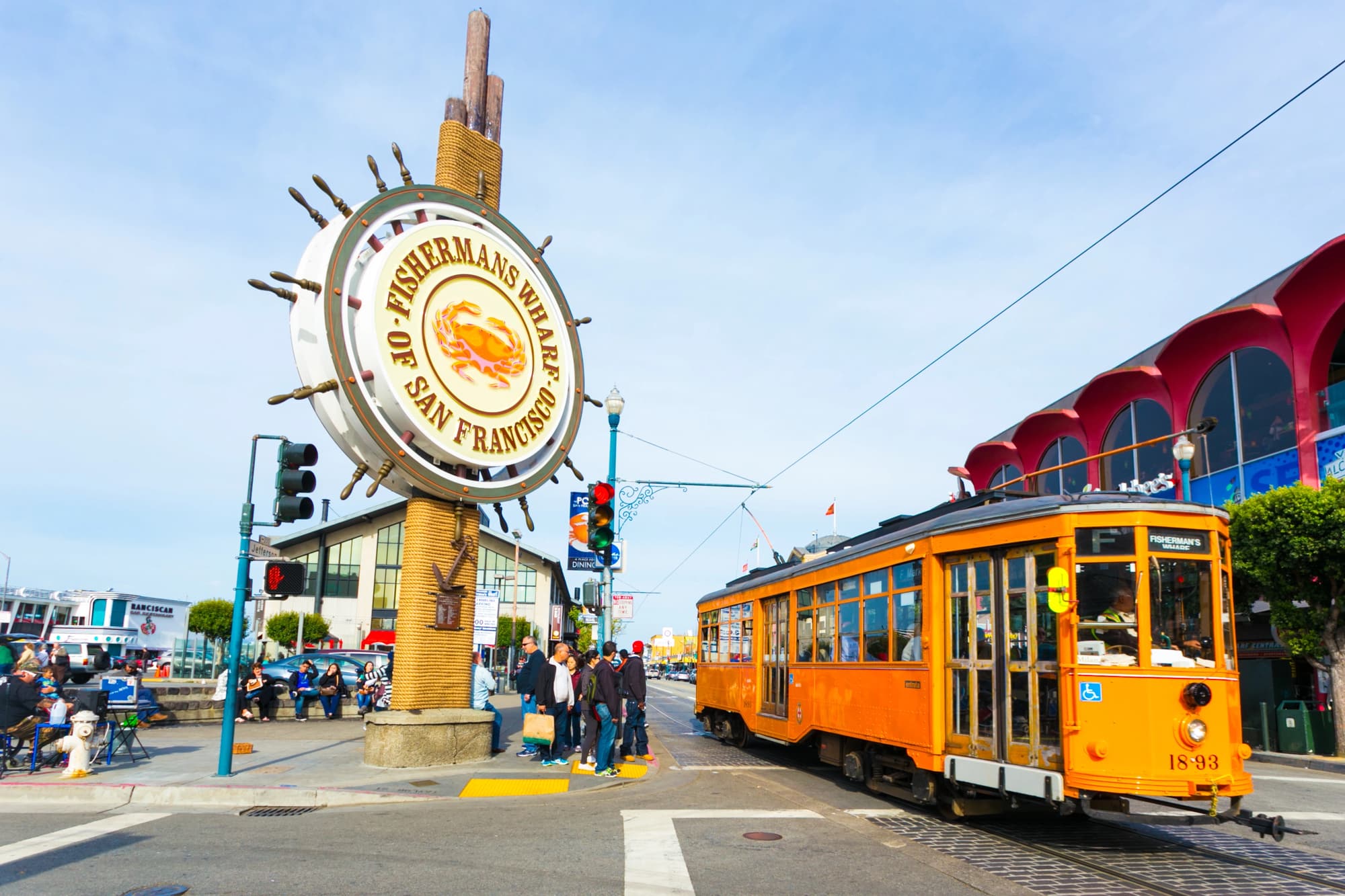 Insegna di Fisherman’s Wharf accanto a un tram arancione e agli edifici sul lungomare