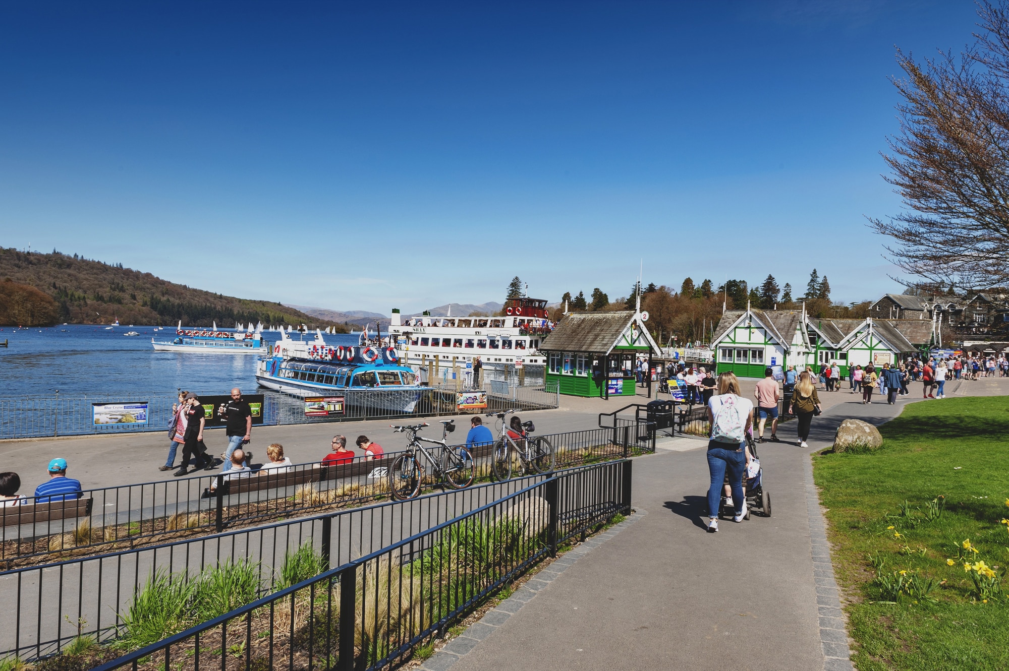 Persone che passeggiano sul lungolago di Bowness-on-Windermere con una barca sul lago