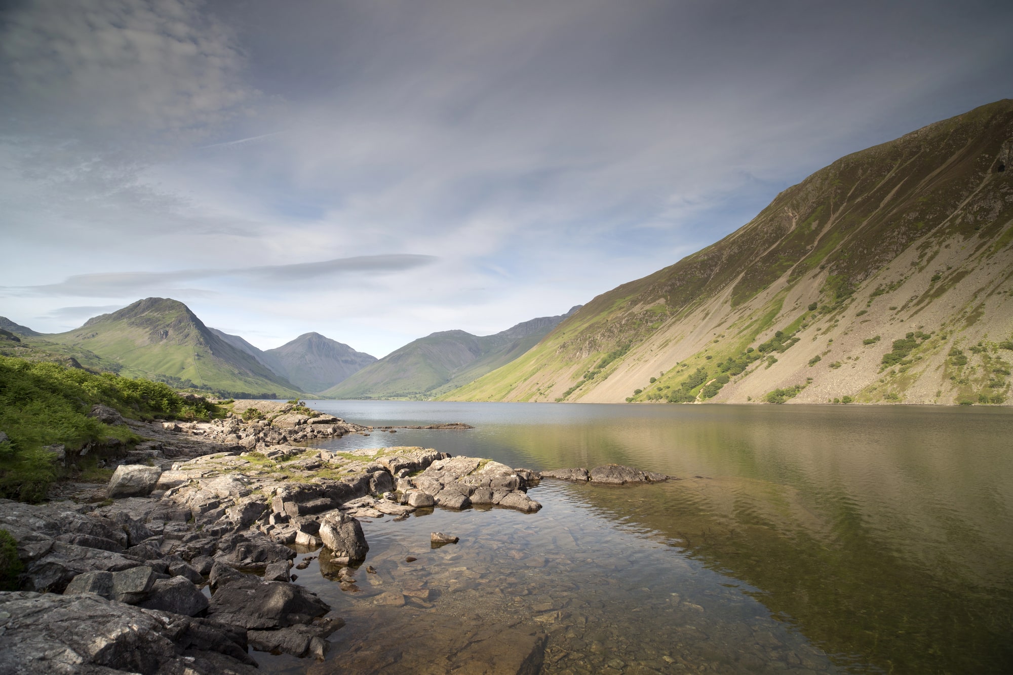 Riva rocciosa di un lago con colline ripide sotto le nuvole nel Lake District