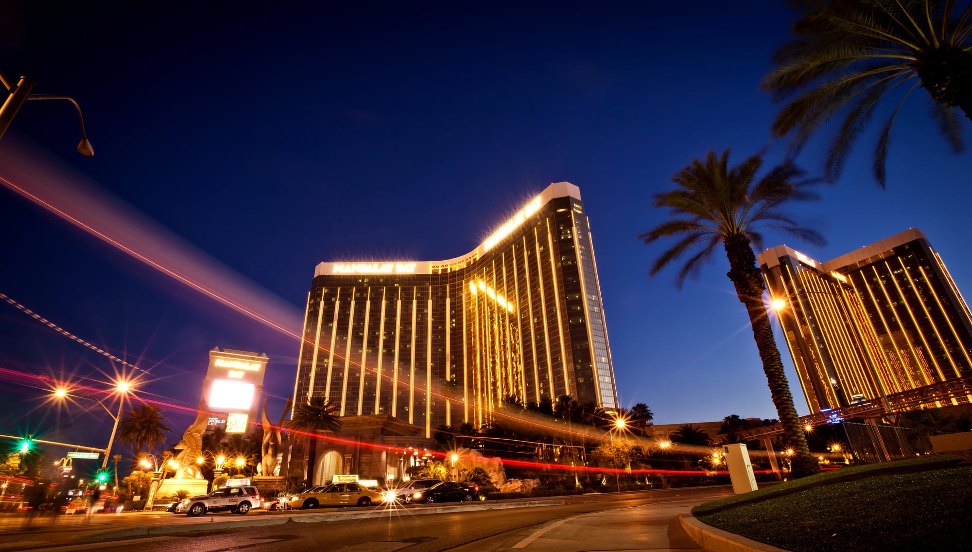 La torre illuminata del Mandalay Bay con palme e traffico di notte