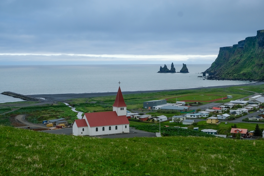 Vík con la sua chiesa, la spiaggia di sabbia nera e i faraglioni di Reynisdrangar sulla costa meridionale dell'Islanda